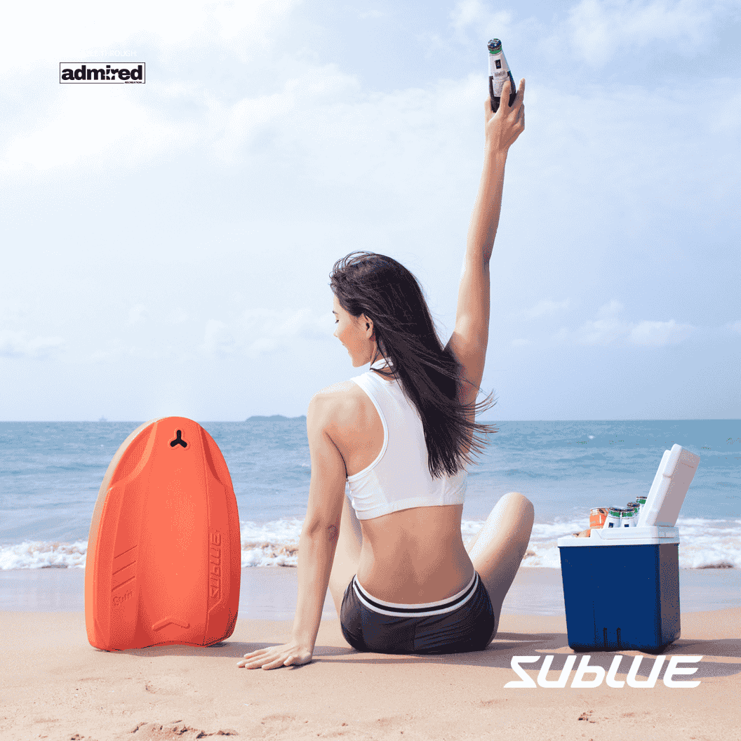 Woman holding SUBLUE Swii kickboard, sitting on the beach by the water.