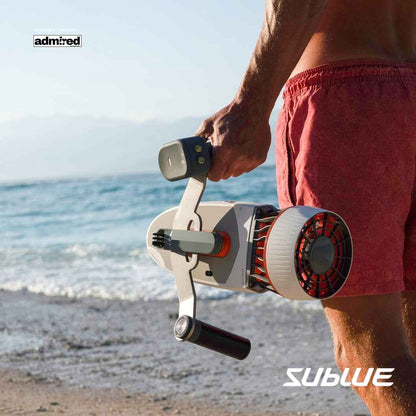 A person in a garment holding a Sublue Tini Underwater Scooter on a beach