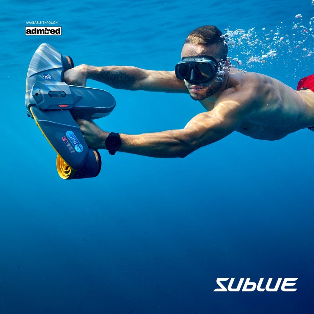 Diver in red shorts using SUBLUE Navbow+ underwater scooter in clear blue water.